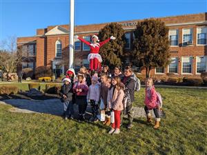 Mrs. Rodriguez sits atop a ladder dressed like the elf on the shelf with students by her